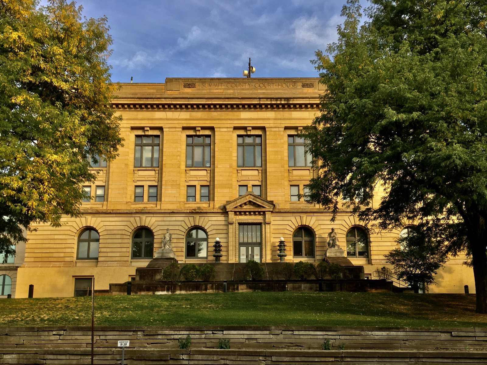 The Summit County Courthouse in Akron, Ohio, a yellow sandstone Renaissance Revival building with arched windows and statues flanking the entrance, framed by trees.